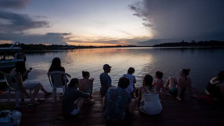 Viajantes assistindo ao pôr do sol à beira do rio