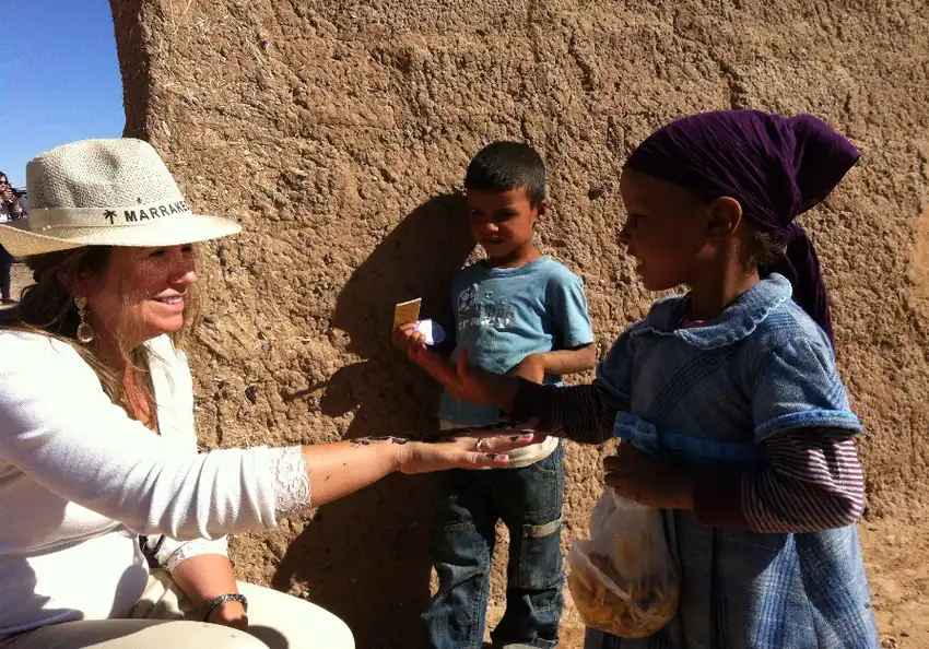 Viajante sorrindo e partilhando um gesto com duas crianças diante de uma parede de barro, no Marrocos